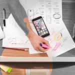 Digital Design and Strategy. A photo from above stylised in partly black and white showing a man with a mobile phone designing a new app.