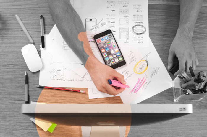 Digital Design and Strategy. A photo from above stylised in partly black and white showing a man with a mobile phone designing a new app.