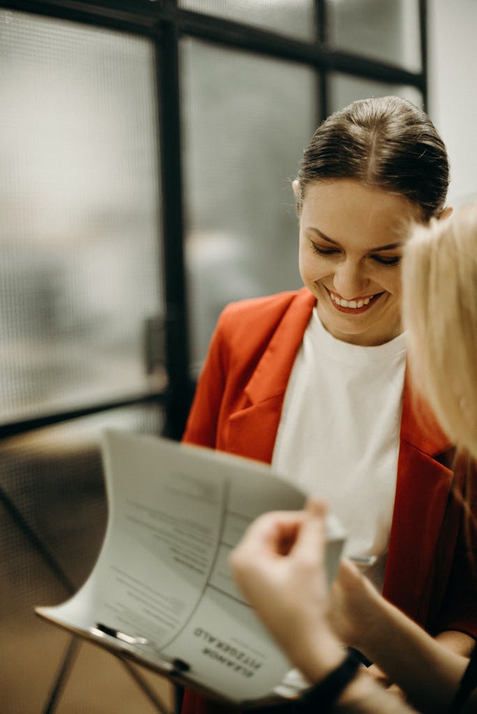 Two young women discussing documents in a modern office environment, smiling and engaged.