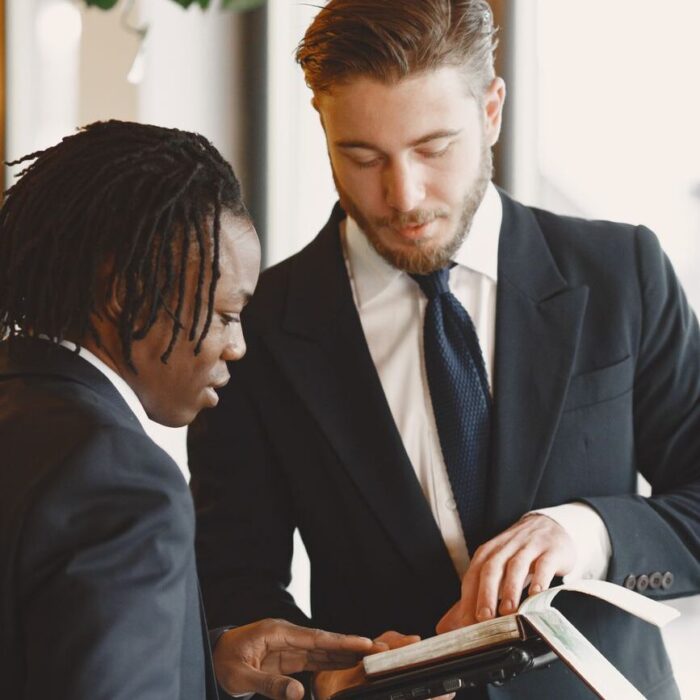 two men in black suits looking at an open book